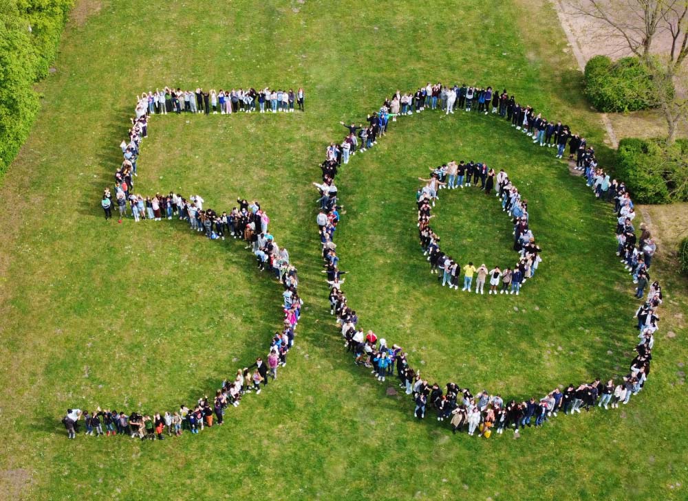 Schüler:innen und das Team des Gymnasium Osterbek formen eine 50 auf einer Wiese von einer Drohne aufgenommen