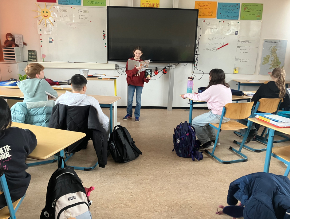 Schülerin liest vor der Klasse aus einem Buch vor