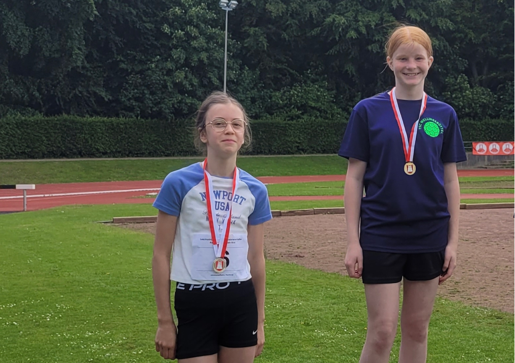 zwei Schülerinnen zeigen ihre Leichtathletikmedaillen