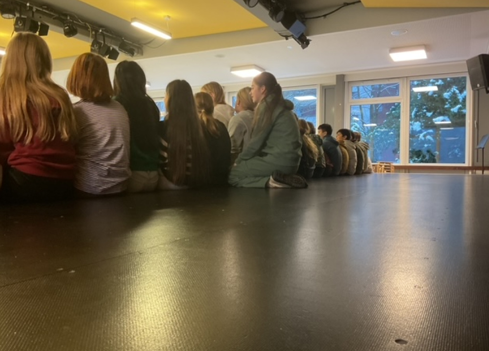 Schüler:innen sitzen am Boden der Aula