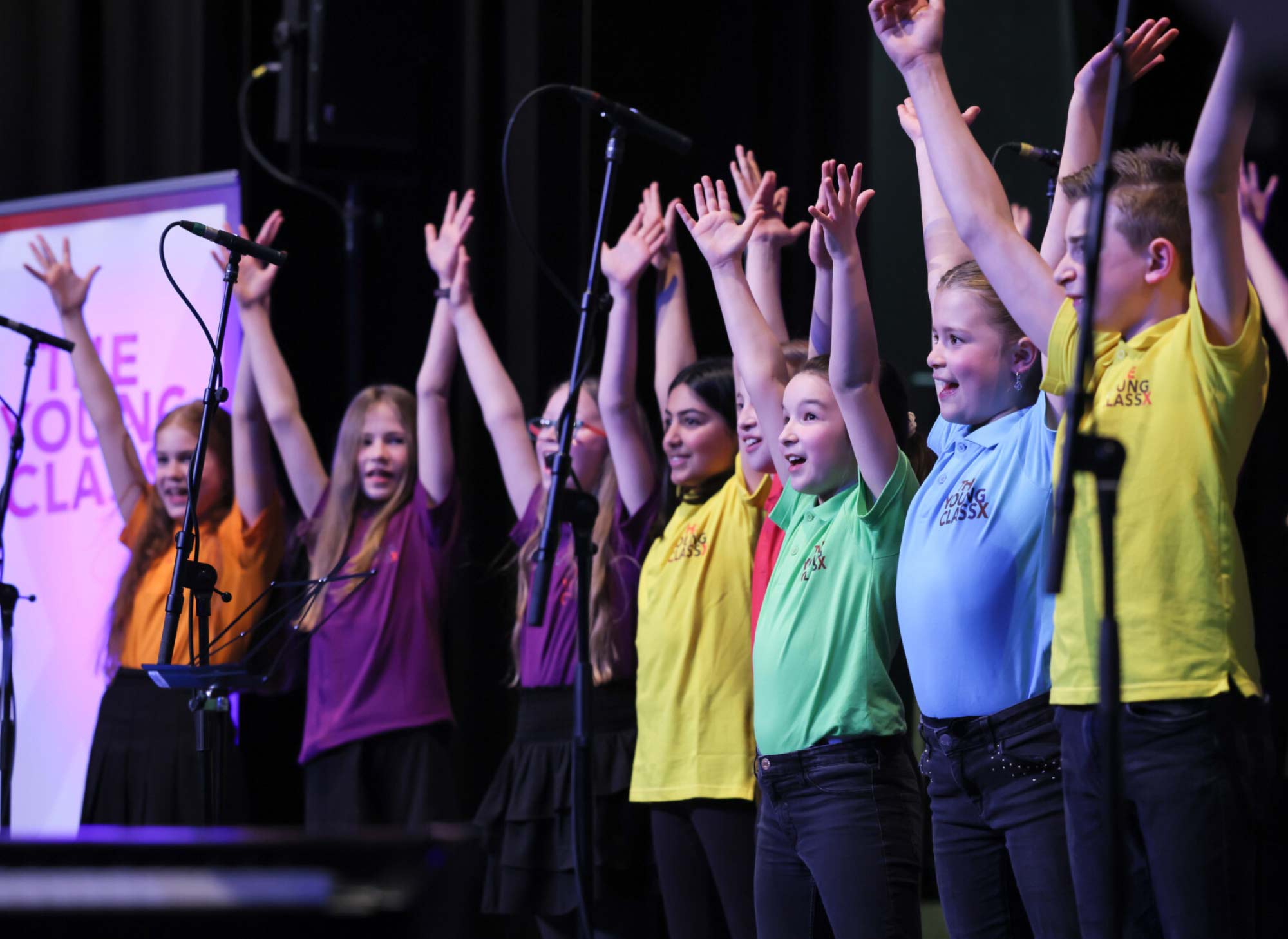 Kinder bei einem Gesangsauftritt auf der Bühne in bunten T-Shirts