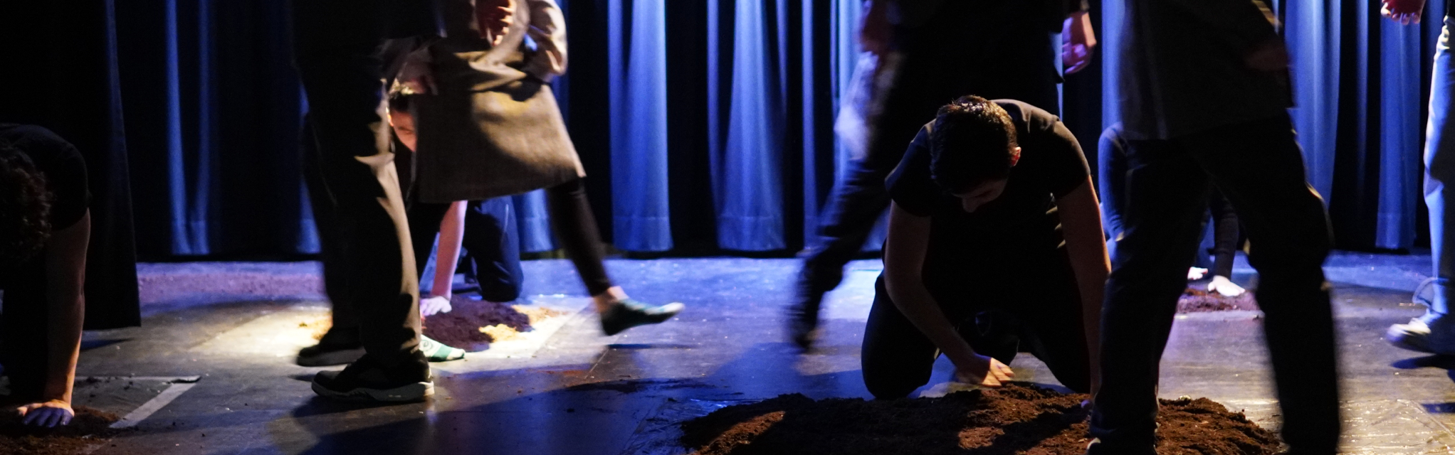 Schüler:innen laufen auf der Bühne, ein Schüler klopft Erde fest