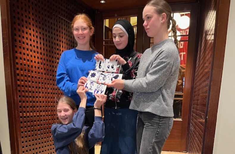 Schülerinnen zeigen Kacheln mit Friedengrüßen der Thalia-Kunstaktion