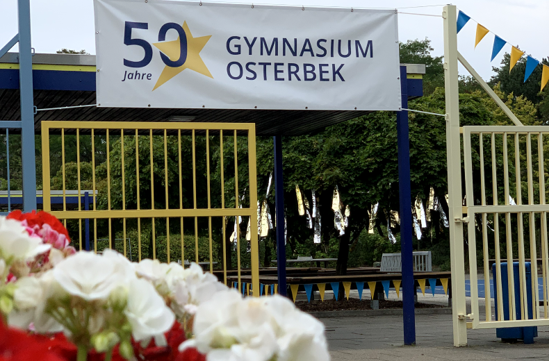 offenes Schultor mit Blumen und Plakat